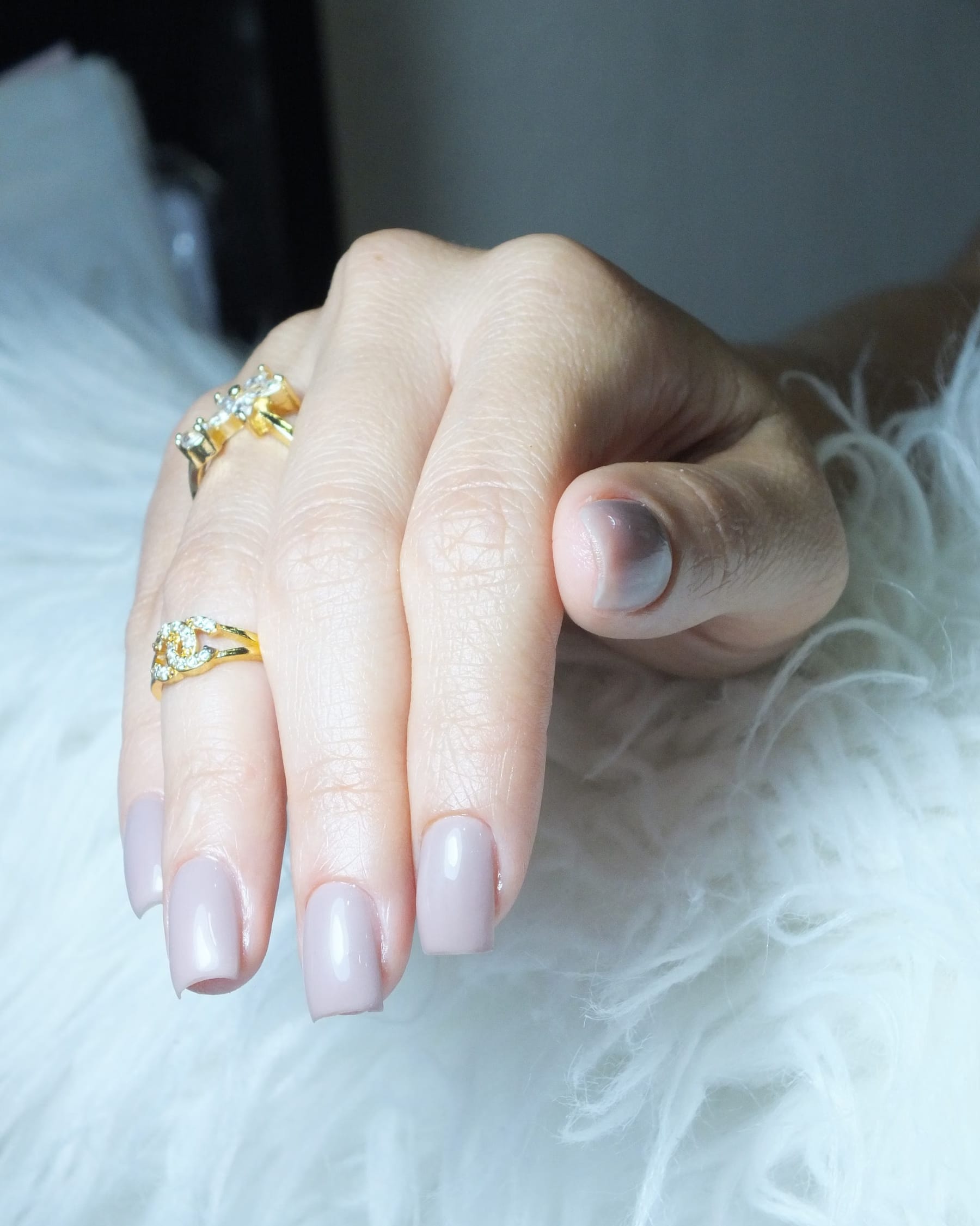 Manicured hands with milky pink gel polish against a sage background